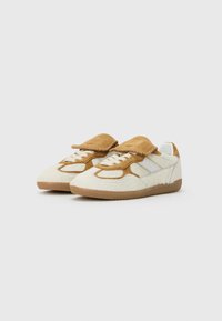 Sneakers featuring a cream furry upper, tan suede accents, laces, and a rubber outsole. Rounded toe and a fold-over flap at the tongue.