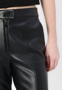 Black faux leather pants with a smooth texture, featuring a front zipper closure and a high waist design.