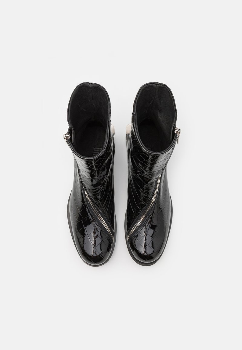 Zwarte enklaarsjes met een glanzend, gestructureerd krokodillenpatroon, voorzien van een diagonale rits en contrasterende beige accenten op de hak.