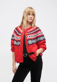 Κόκκινη πλεκτή ζακέτα με μοτίβο Fair Isle σε λευκό και ναυτικό μπλε, με στρογγυλή λαιμόκοψη και μεγάλα καφέ κουμπιά. Μαλακό, υφασμάτινο ύφασμα με υφή.