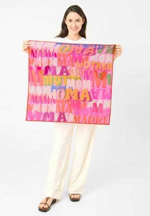 Smiling woman holding a pink scarf with colorful words like "MOM," "MAMA," "MOTHER," and "MADRE" in varied fonts and sizes.