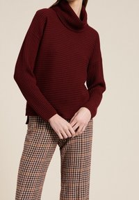 Burgundy ribbad polotröja med långa ärmar, ihopparad med bruna och beige rutiga byxor i hundtandsmönster. Mjuk textur, avslappnad passform.