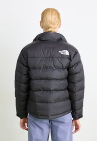 Schwarze Daunenjacke mit hohem Kragen, gestepptem Muster und Logo auf dem Rücken. Glattes, glänzendes Material mit gepolsterter, isolierter Verarbeitung.