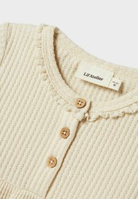 Maglione beige a trama con design a coste, colletto rotondo, volants decorativi e tre bottoni in legno. L'etichetta riporta "Lil' Atelier" e la taglia.