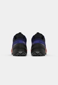 Vista traseira dos sapatos Salomon Speedcross 6, apresentando um cabedal azul-marinho, detalhes em preto e uma sola texturizada com pormenores em vermelho e elementos de marca.