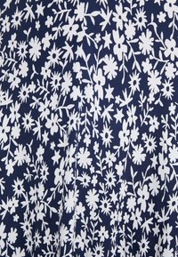 Motif dense de petites fleurs blanches et de feuilles sur un fond de tissu bleu foncé, créant un design textile floral.