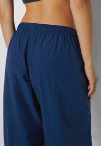 Navy blue lightweight trousers with an elastic waistband, featuring a relaxed fit and smooth textured fabric.