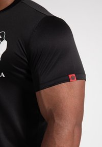 Black athletic shirt made of smooth fabric, featuring a white graphic on the front and a red logo tag on the sleeve.