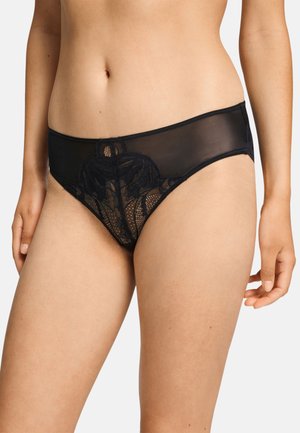 Vrouw draagt zwart kanten en mesh hipster-stijl ondergoed met bloemenpatroon op het voorpaneel, getoond van taille tot bovenbenen.