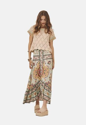 Top de punto rosa con patrón de diamantes, combinado con una falda maxi multicolor con motivos florales, dobladillo en capas y sandalias de plataforma beige.