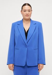 Blazer entallado azul hecho de una tela suave. Presenta solapas con muesca, cierre de un solo botón y dos bolsillos frontales con costuras sutiles.