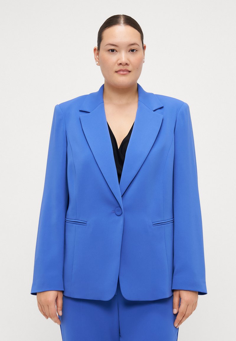 Blazer entallado azul hecho de una tela suave. Presenta solapas con muesca, cierre de un solo botón y dos bolsillos frontales con costuras sutiles.