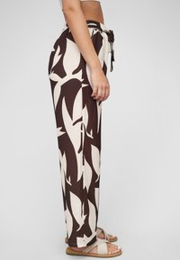 Pantalons larges marron avec un motif abstrait de feuilles crème. Fabriqués dans un tissu léger, avec une taille élastique et un détail de lien.