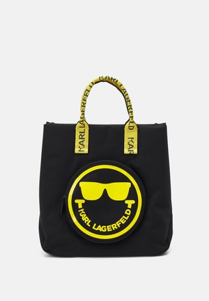 Cabas noir avec anses jaunes et poche avant illustrée d’un graphisme rond jaune représentant des lunettes de soleil et le texte « KARL LAGERFELD ».