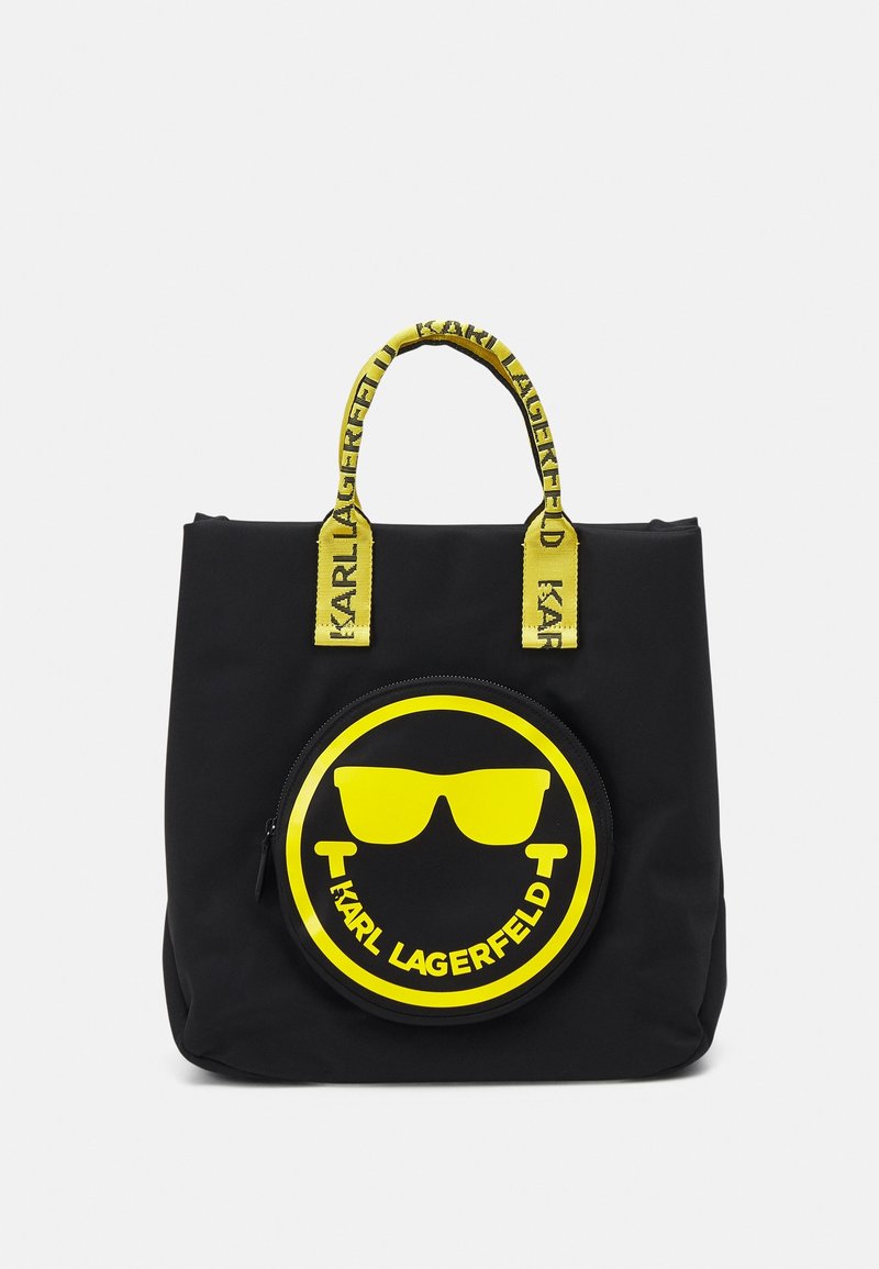 Cabas noir avec anses jaunes et poche avant illustrée d’un graphisme rond jaune représentant des lunettes de soleil et le texte « KARL LAGERFELD ».