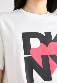 Biała bawełniana koszulka z dużym czarnym napisem "DK" i czerwonym sercem, krótki rękaw i okrągły dekolt. Gładka tekstura i swobodny krój.