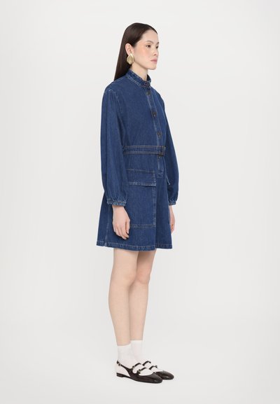 Rochie din denim cu guler, nasturi pe partea din față, talie cu curea și două buzunare mari. Culoare albastru deschis, mâneci lungi și bufante, lungime până la genunchi.