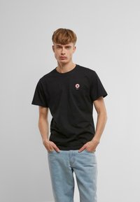 Sort bomulds t-shirt med et lille pink donut grafik på brystet, parret med lyseblå denim jeans. Simpel crew neckline og korte ærmer.