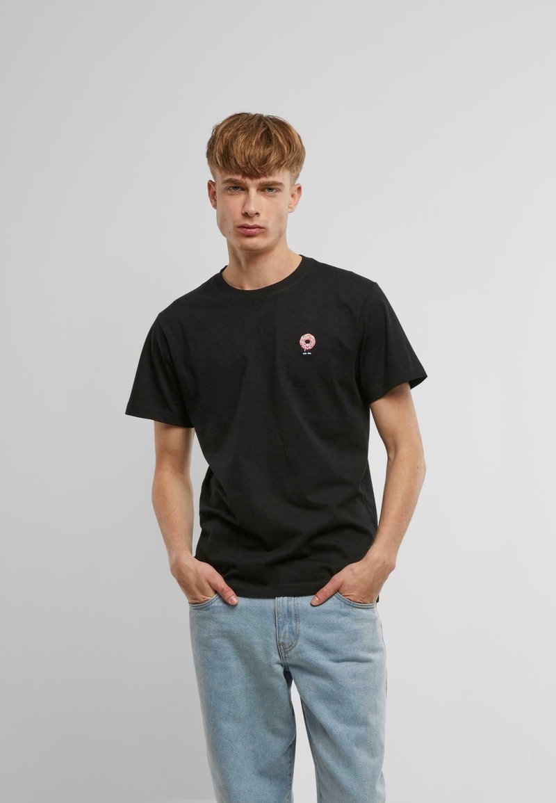 Sort bomulds t-shirt med et lille pink donut grafik på brystet, parret med lyseblå denim jeans. Simpel crew neckline og korte ærmer.