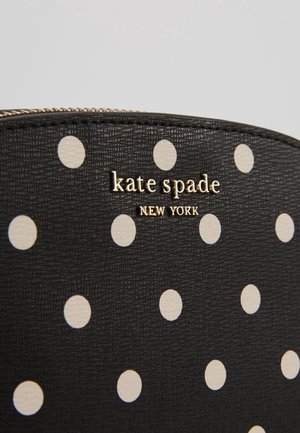 Czarny teksturowany woreczek z białymi kropkami i złotym logo „kate spade NEW YORK” blisko góry, suwak widoczny nad logo.