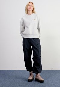 Szary sweatshirt z małym logo, połączony z czarnymi spodniami cargo i beżowymi butami na sznurówki z grubą czarną podeszwą. Płaskie tło.