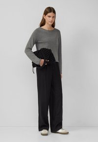 Grijze lange mouwen top, zwarte wijde broek en een zwarte tas met structuur en een handvat. De schoenen zijn wit met beige accenten.