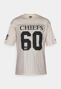 Μπεζ δικτυωτή φανέλα ποδοσφαίρου με το "CHIEFS" σε μαύρο χρώμα, τον αριθμό "60" κεντραρισμένο και το "EST" από κάτω. Λογότυπο NFL στον αριστερό αυχένα.