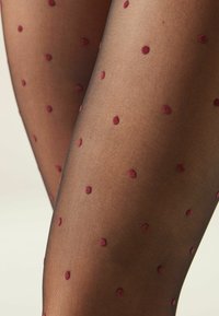 Durchsichtige schwarze Strumpfhosen mit einem gepunkteten Muster aus kleinen burgunderfarbenen Punkten. Die Textur ist glatt und leicht transparent.