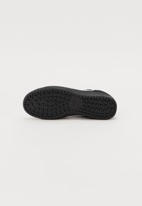 Semelle en caoutchouc noir d'une basket avec motif de bande de roulement carré et petit logo Nike au centre sur fond blanc.