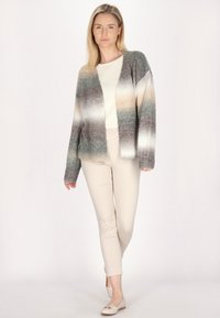 Cardigan lavorato a maglia in sfumature di grigio, beige e verde, con maniche lunghe, apertura frontale e polsini a coste, abbinato a pantaloni beige chiaro.