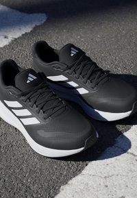 Black athletic shoes with white accents, featuring a textured finish, sturdy laces, cushioned collar, and a distinctive logo on the tongue.