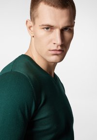 Zielony sweter z dzianiny z dekoltem w kształcie litery V, dopasowanym kroju i teksturowanym materiałem. Posiada gładkie wykończenie i delikatne szwy.