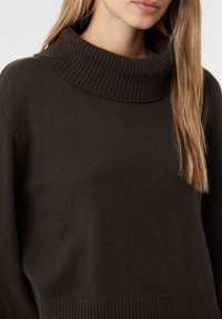 Brauner Strickpullover mit einem gerippten Funnel-Neck und langen Ärmeln. Weiche Textur und lockere Passform, mit einem gerippten Saum für zusätzliche Details.