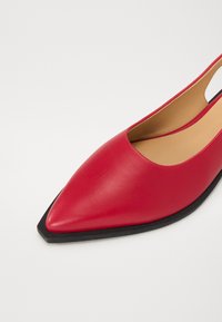Scarpe flat in pelle rossa con punta affilata, lati tagliati e suola in gomma nera. Texture liscia e design minimalista.