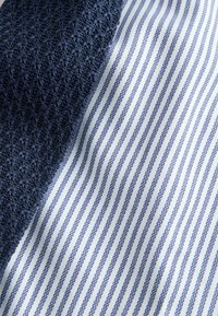 Gros plan sur un tissu bleu marine texturé à côté d'un tissu blanc avec de fines rayures verticales bleues.