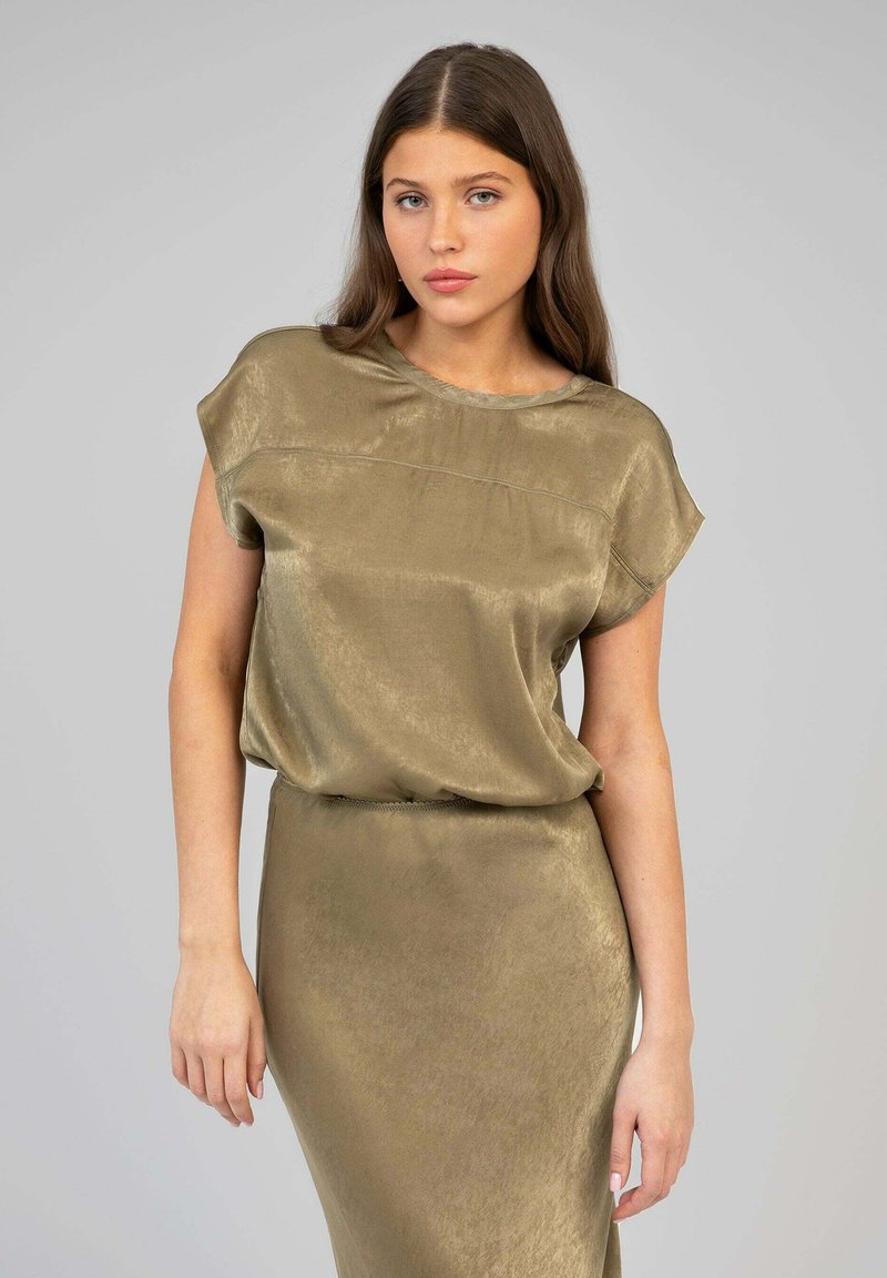 Haut olive, à manches courtes, avec une texture lisse et brillante et un col arrondi, associé à une jupe moulante assortie.