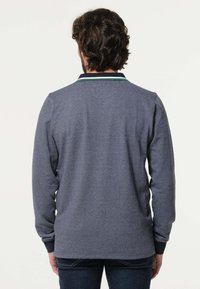 Donkerblauwe polo met lange mouwen, voorzien van een contrasterende zwarte en groene geribde kraag en manchetten, gemaakt van een zachte, gestructureerde stof.