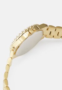 Reloj de pulsera dorado con una correa de metal pulido, caja redonda y un bisel con incrustaciones. Presenta una corona simple en el lateral y una parte trasera lisa.