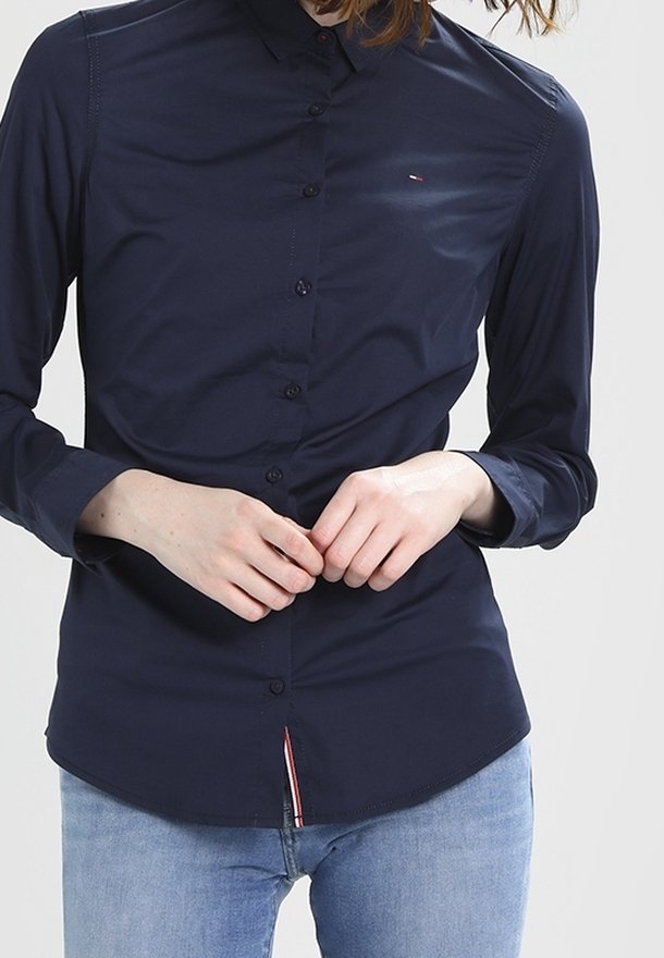 Námořnická modrá košile na knoflíky vyrobená z hladké látky, s límečkem, dlouhými rukávy a červenobílým akcentem na spodním lemu.