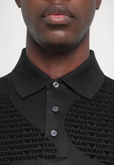 Svart poloskjorte med strukturert krage, to-knappslukking og et tonalt mønster av merket over stoffet.