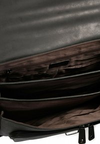 Interno di una borsa in pelle nera con texture liscia, dotato di tre scomparti, una tasca con zip e fodera in tessuto marrone.