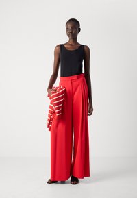 Zwarte tanktop, rode wijde broek, houdt een gestreepte trui in rood en wit vast. Gladde stof, gestructureerde silhouet, casual ontwerp.