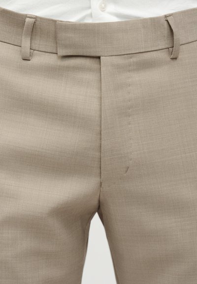 Μπεζ παντελόνι με ίσια γραμμή στο μπροστινό μέρος. Διαθέτει ομαλή υφή, θηλιές για τη ζώνη και ραφή στο τελείωμα των ποδιών.