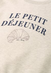 Tissu beige avec texte bleu marine "LE PETIT DÉJEUNER" et une illustration de croissant gris clair avec un petit texte "Mon Paris" en dessous.