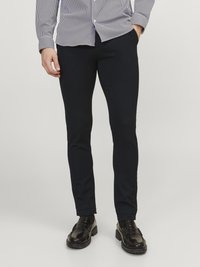 Navyblaue, figurbetonte Hose aus einem Baumwoll-Mix mit glatter Textur und minimalistischem Design. Getragen mit schwarzen Slippern und einem gestreiften Hemd.