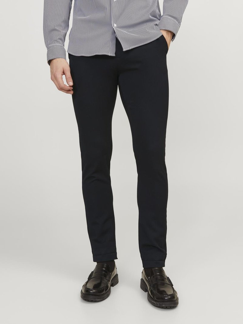 Navyblaue, figurbetonte Hose aus einem Baumwoll-Mix mit glatter Textur und minimalistischem Design. Getragen mit schwarzen Slippern und einem gestreiften Hemd.