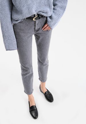 Light blue knitted sweater, gray tapered jeans, black loafers with chain detail, and a black belt with a circular buckle.
