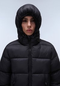 Sort pufferjakke med quiltet design, der har høj krave og hætte. Fremstillet af et skinnende, glat materiale med snoretrækjusteringer.