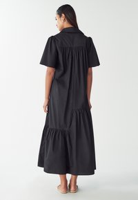 Čierne bavlnené šaty s krátkymi balónovými rukávmi, golierom, nariasenými detailmi a dizajnom s viacerými sukňami, dosahujúce do polovice lýtok.