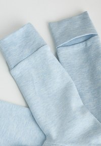 Manches en tissu doux bleu clair avec larges poignets côtelés, étalées à plat sur une surface blanche.